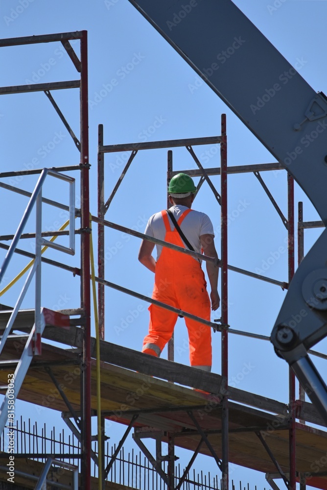 a male builder in an orange suit and a helmet stands at a construction site