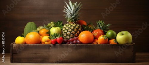 Wooden box with a variety of fruits pineapple garnet tangerine apple and kiwi There is also free copy space in the background