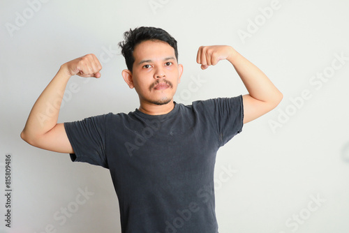 Adult Asian man showing excited expression by showing up his biceps muscle photo