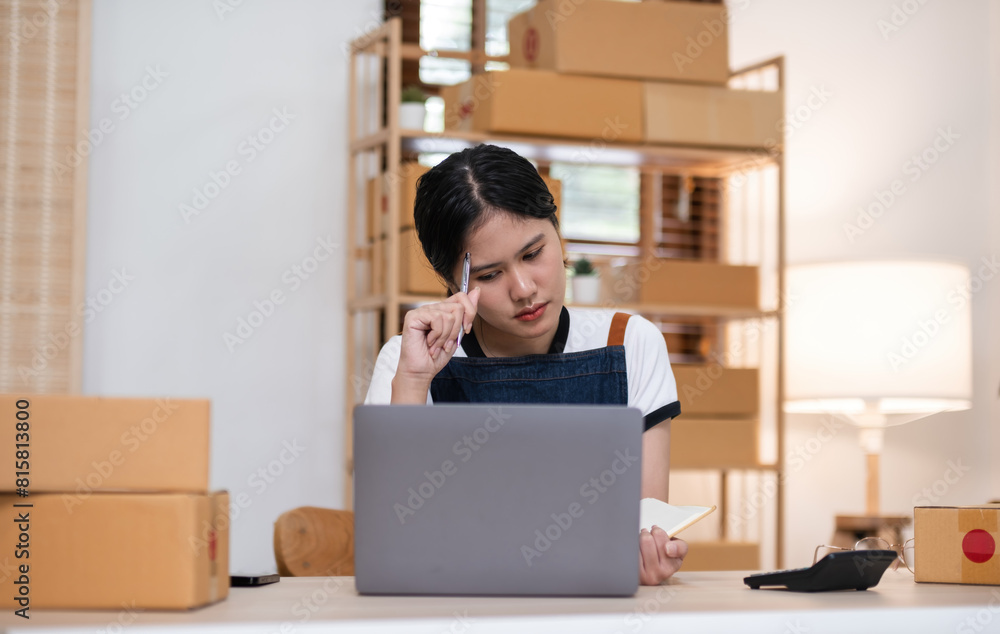 A small SME business owner feels tired while sitting on his home desk packing products into boxes. A small SME business owner feels tired while sitting on his home desk packing products into boxes.