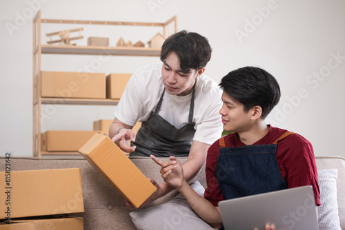 A gay couple running a small business takes order on a laptop and sells product online together in a room full of boxes. © wichayada