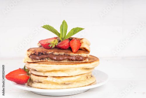 Stack of chocolate nutella filled pancakes. Sweet breakfast pancakes with chocolate sauce inside it, and fresh stawberries, on white kitchen table