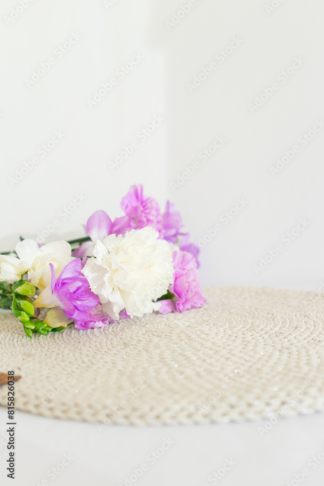 Beige wicker table napkin and purple and white carnation flowers close up. Handmade round tablecloth. Organic tableware Beige wicker table napkin and purple and white carnation flowers close up. Handmade round tablecloth. Organic tableware