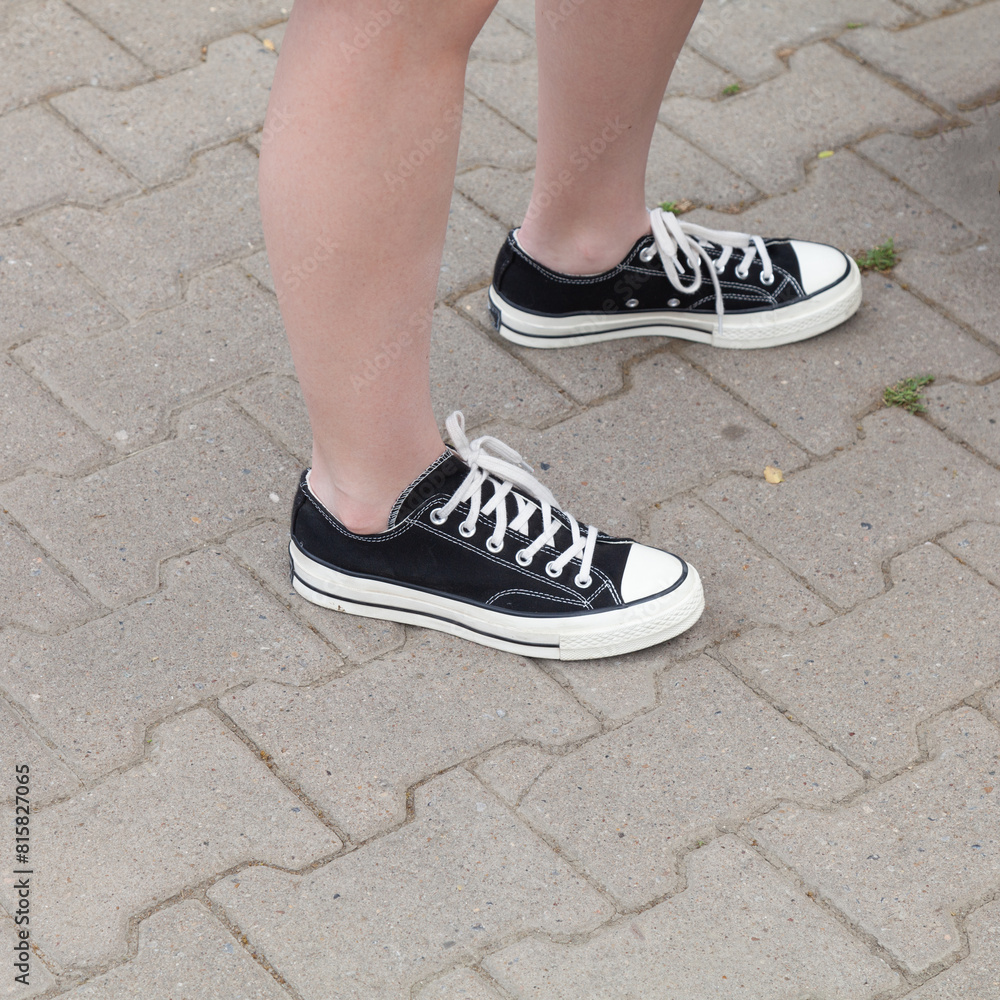 Black casual shoes.Feet of a teenager in black canvas shoes stand on an asphalt road