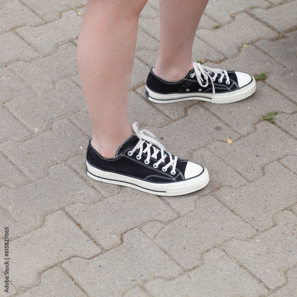 Black casual shoes.Feet of a teenager in black canvas shoes stand on an asphalt road Black casual shoes.Feet of a teenager in black canvas shoes stand on an asphalt road