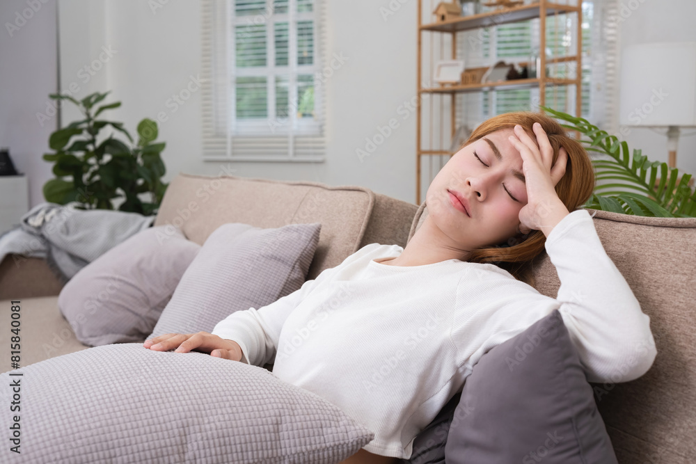 A young Asian woman in the living room was suffering from a headache due to accumulated stress due to health problems and lifestyle problems causing stress disorder. A young Asian woman in the living room was suffering from a headache due to accumulated stress due to health problems and lifestyle problems causing stress disorder.