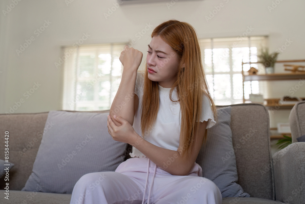 Young woman examining her arm indoors, feeling discomfort Young woman examining her arm indoors, feeling discomfort