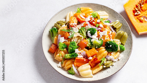 Autumn pasta salad with roasted pumpkin, broccoli, feta cheese on bright light background, fall season salad