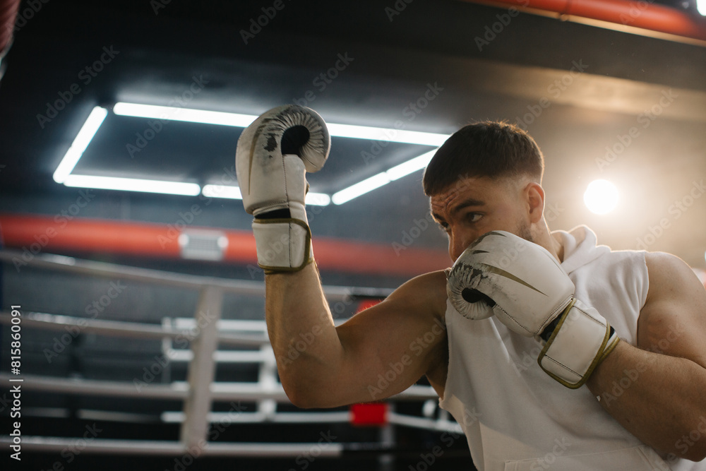 A male boxer is boxing with a shadow on the background of a boxing ring. A boxer practices his punches in a boxing studio.