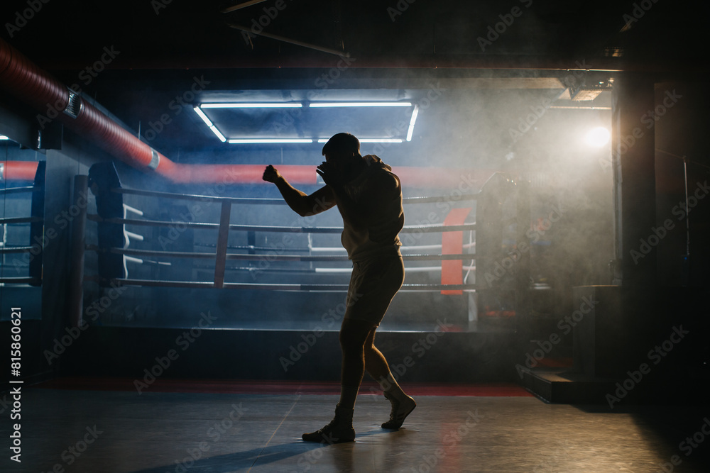 A male boxer is boxing with a shadow on the background of a boxing ring. A boxer practices his punches in a boxing studio. A male boxer is boxing with a shadow on the background of a boxing ring. A boxer practices his punches in a boxing studio.