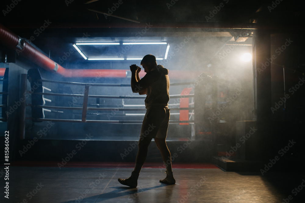 A male boxer is boxing with a shadow on the background of a boxing ring. A boxer practices his punches in a boxing studio. A male boxer is boxing with a shadow on the background of a boxing ring. A boxer practices his punches in a boxing studio.