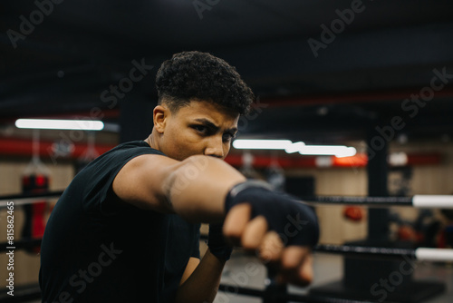 A focused young boxer practices his punches. Sporty young man training in boxing gym.