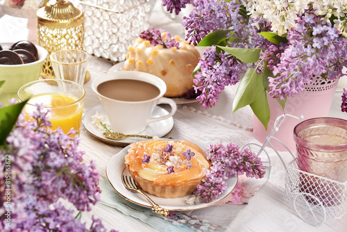 Sweet tartlet and a cup of coffee on the table decorated with lilac blossoms © teressa