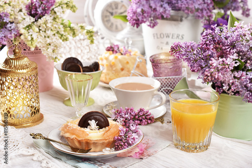 Sweet tartlet and a cup of coffee on the table decorated with lilac blossoms