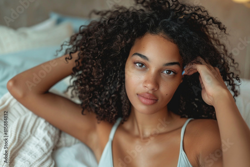 African curly-haired woman embraces the Curly Girl Method, tenderly combing her locks in a bedroom scene, epitomizing the care and beauty of natural curls.