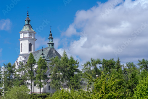 Zabytkowy kościół (kolegiata) św. Michała Archanioła w słoneczny wiosenny dzień. Kilkusetletnia świątynia katolicka wśród wiosennej zieleni na wzgórzu pod błękitnym niebem w Ostrowcu.
