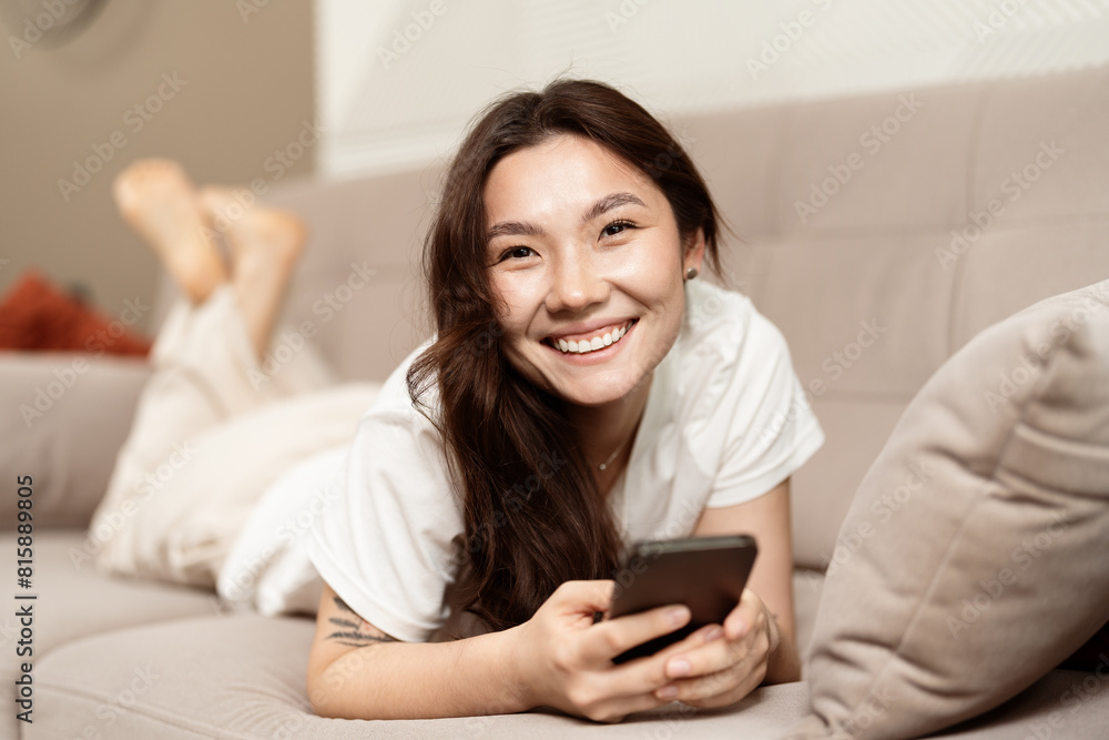 Happy Young Woman Relaxing On Couch With Smartphone, Enjoying Leisure Time At Home, Cheerful Expression, Casual Comfort Happy Young Woman Relaxing On Couch With Smartphone, Enjoying Leisure Time At Home, Cheerful Expression, Casual Comfort