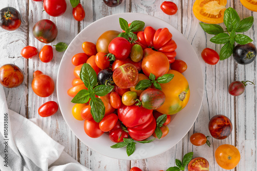 A mix of ripe multi-colored organic tomatoes with fresh basil on a plate on old wooden background. Healthy food.