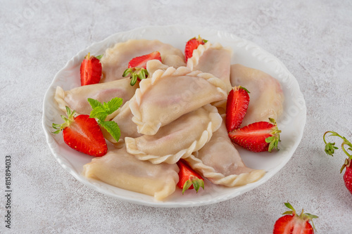 Tasty traditional dumplings, varenyky or pierogi with strawberry and sour cream on a white plate.