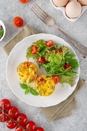 Egg muffins or egg bites with bacon, cheese, vegetables and herbs on a white plate on a concrete background. Healthy breakfast.