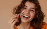 A woman with dark brown hair is smiling and holding an Inaw mini aligner in front of her mouth, showing off the transparent braces on it.