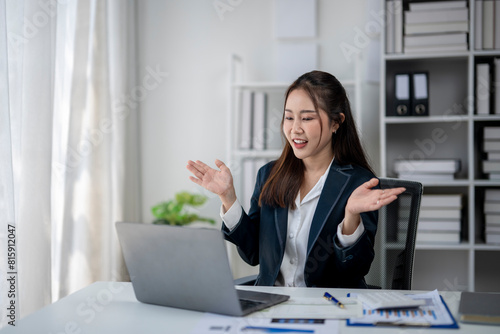 A woman in a business suit is sitting at a desk with a laptop open. She is smiling and she is happy