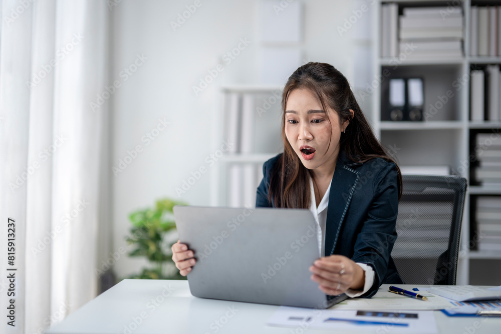A woman in a business suit is looking at a laptop screen with a surprised expression on her face A woman in a business suit is looking at a laptop screen with a surprised expression on her face