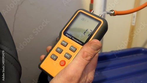Gas engineer measuring pressure holding in his hand portable digital manometer connected to domestic piping or pipework, close up shot.