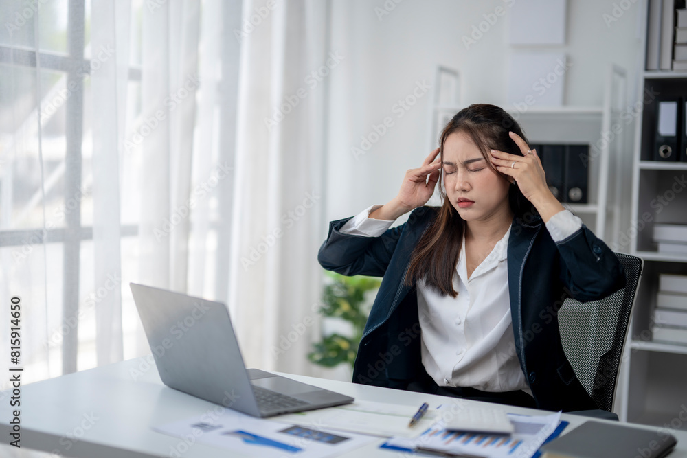 A woman is sitting at a desk with a laptop and a stack of papers. She is wearing a black suit and she is in a state of stress or frustration A woman is sitting at a desk with a laptop and a stack of papers. She is wearing a black suit and she is in a state of stress or frustration