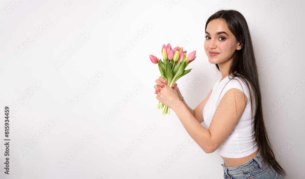 Young brunette woman posing isolated over white wall background holding flowers Young brunette woman posing isolated over white wall background holding flowers