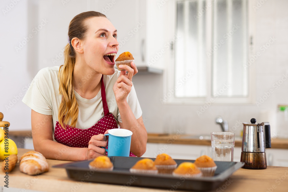 Woman in apron tasting freshly baked sweet cupcakes in kitchen Woman in apron tasting freshly baked sweet cupcakes in kitchen