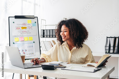 A woman is sitting at a desk with a laptop and a book