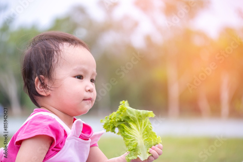 Little asian girl in the garden. kid playing outdoors in summer day. child eating vegetables. Copy space.