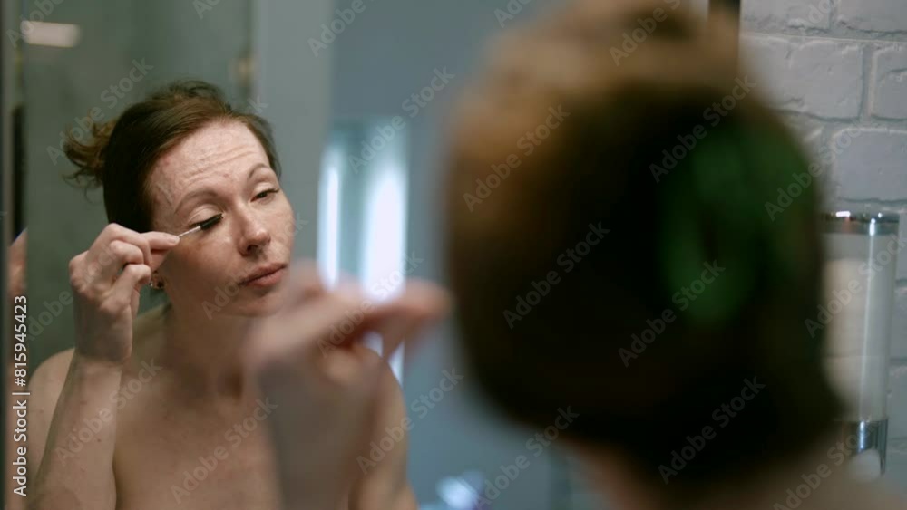 In the cozy atmosphere of her bathroom, an adult woman takes care of her beauty, attaching importance to details and accuracy when using an eyelash comb. In the cozy atmosphere of her bathroom, an adult woman takes care of her beauty, attaching importance to details and accuracy when using an eyelash comb.