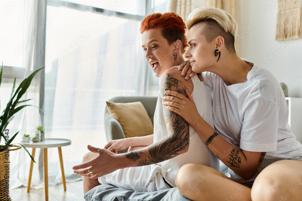 Two edgy women with tattoos sitting closely on a cozy couch in a stylish living room. Two edgy women with tattoos sitting closely on a cozy couch in a stylish living room.