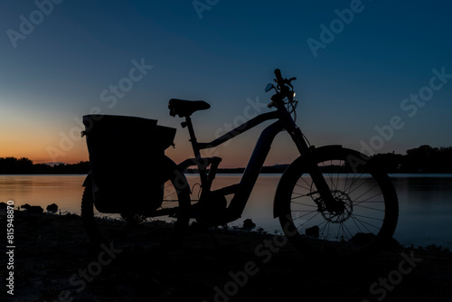 Silhouette of electric bicycle on beach of pond Bezdrev after sunset