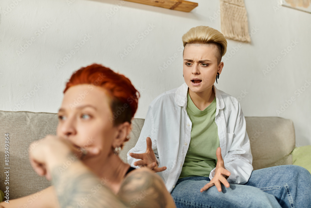 Fototapeta premium Two women with short hair sitting on a couch, engaged in emotional conversation at home.