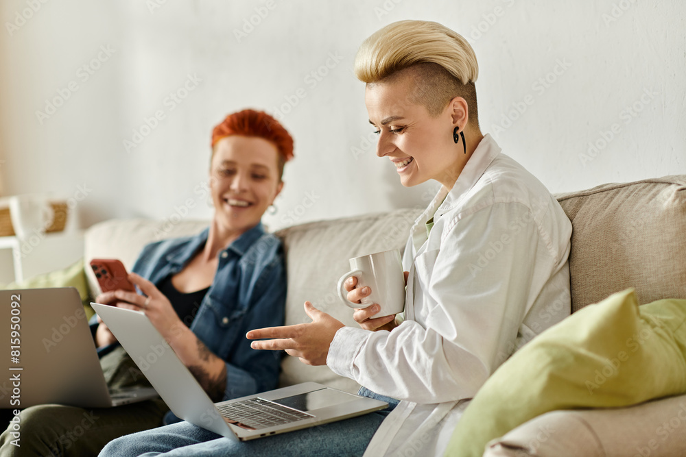 Two women, a lesbian couple with short hair, sit closely on a couch, each focused on their laptops, possibly working or sharing ideas. Two women, a lesbian couple with short hair, sit closely on a couch, each focused on their laptops, possibly working or sharing ideas.