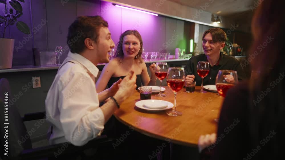 Group of friends talking in night bar. Young cheerful girl emotionally tells the story to friends laughing drinking alcohol cocktails, sitting at table, having fun together. Party friendship concept. Group of friends talking in night bar. Young cheerful girl emotionally tells the story to friends laughing drinking alcohol cocktails, sitting at table, having fun together. Party friendship concept.