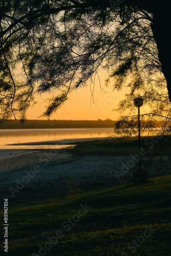 Obraz na płótnie Sunset on the lake shore with tree silhouette and lighthouse w salonie
