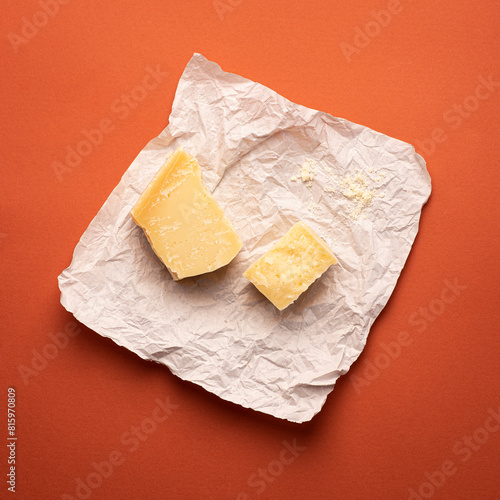 Grana Padana cheese on a piece of paper. Aged cheeses of Northern Italy. Terracotta background