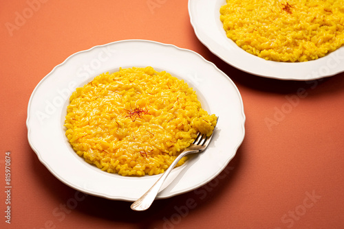 Risotto alla Milanese in a white aristocratic dish on the terracotta color table. A classic Lombard saffron risotto recipe. Cuisine the North Italy. Front viw