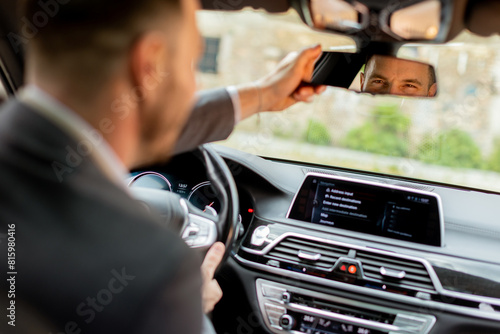 Businessman adjusting rearview mirror before commuting in modern vehicle photo