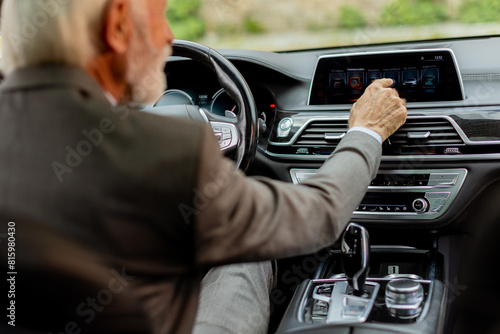 Senior gentleman adjusting the touchscreen panel in a modern car interior during daytime drive photo