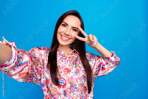 Photo of positive cute lady dressed print blouse recording video showing v-sign isolated blue color background photo