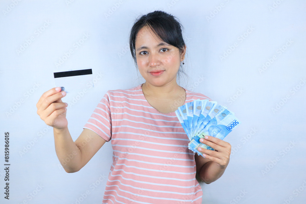Portrait of a smiling asian young woman holding cash rupiah and credit card on white background Portrait of a smiling asian young woman holding cash rupiah and credit card on white background