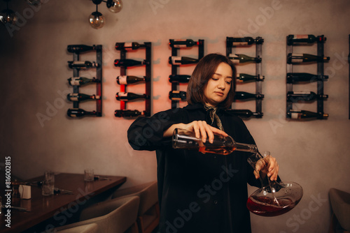 Fotografija Female sommelier pouring red wine into long-stemmed wineglass, close up indoor portrait