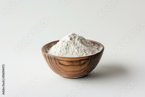 Wooden bowl filled with white baking flour positioned on a neutral backdrop