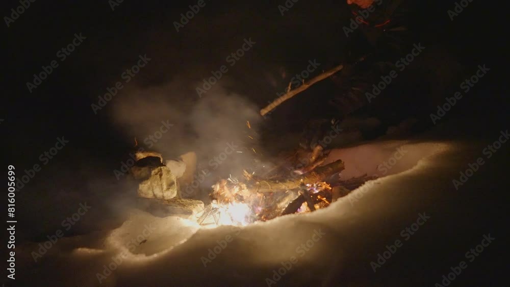 A man is seen warming his hands by a carefully-made campfire surrounded by snow, under the dark night sky. A man is seen warming his hands by a carefully-made campfire surrounded by snow, under the dark night sky.