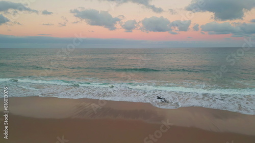 Aerial serene beach sunset view. Waves gently meeting sandy shore in evening
